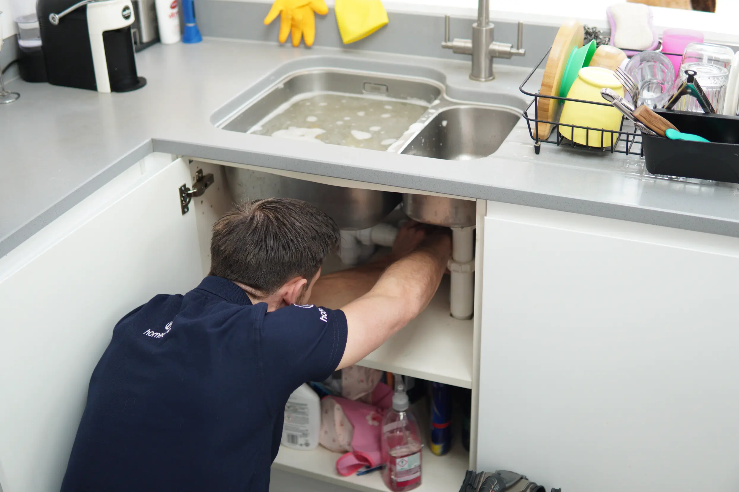 A Homecure plumber fixing a leaking sink